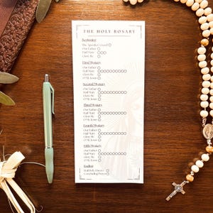 Pode incluir: Um cartão impresso intitulado "THE HOLY ROSARY" com uma lista de orações, ao lado de uma caneta verde clara e um rosário. O cartão tem uma borda decorativa e uma imagem fraca de uma figura religiosa. O rosário tem contas de madeira e um crucifixo de prata.