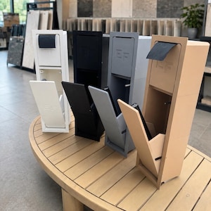 May include: Four vertical wall-mounted dispensers in white, black, grey, and beige, each featuring a top compartment with a flap and a lower section with an angled door. The letters EF are embossed on the upper front of each unit.