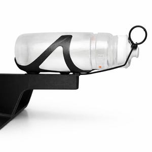 Peut inclure: Une gourde transparente avec un bouchon blanc est maintenue dans un porte-bouteille noir. Le porte-bouteille est monté sur un support noir. Le porte-bouteille a un design en fibre de carbone. La gourde est conçue pour le cyclisme.
