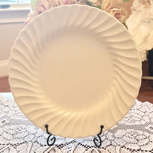 May include: Cream-colored ceramic plate with a spiral design. The plate is displayed on a black metal stand, showcasing its textured surface. The plate's design adds a touch of elegance to any table setting.