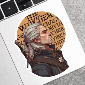 May include: A round sticker featuring a side profile of a man with white hair, wearing a black jacket and a silver medallion. The sticker has the text "THE WITCHER" and other text in a circle around the man.