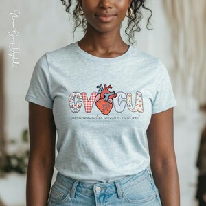 Könnte beinhalten: Hellblaues T-Shirt mit den Buchstaben "CV ICU" in dekorativer Schrift, mit einer Herzgrafik. Der Text "cardiovascular intensive care unit" steht darunter. Das T-Shirt ist aus einem weichen Material.