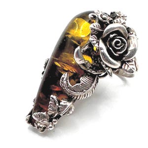 May include: A silver ring featuring a large amber stone and a detailed floral design with a rose.