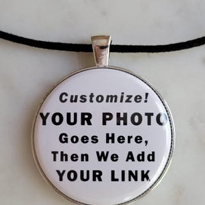 May include: A round, silver-toned pendant necklace with a black cord. The pendant has a white background with the words "Customize! YOUR PHOTO Goes Here, Then We Add YOUR LINK" in black text.