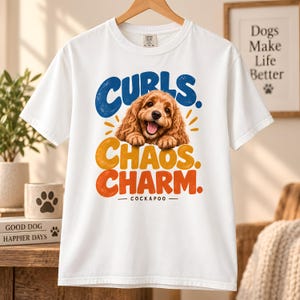 May include: A white short-sleeve t-shirt featuring a graphic of a brown Cockapoo puppy with the text "CURLS. CHAOS. CHARM. COCKAPOO" in blue, yellow, and orange. The puppy is shown with its front paws resting, and the design has a distressed texture.