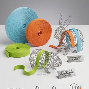May include: Three rolls of light blue, orange, and lime green webbing straps next to wire rabbit and guinea pig models. Text includes AVAILABLE FOR RABBIT, AVAILABLE FOR GUINEA PIG 11cm MODEL, AVAILABLE IN: MULTIPLE SIZES, DURABLE & SOFT WEAVE, AVAILABLE HARNESS COLOURS.