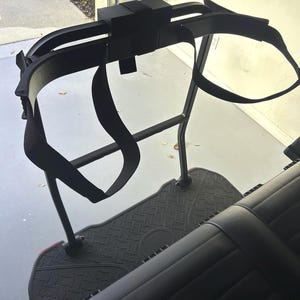 May include: Black golf cart seat with a black frame and a black harness system. The seat has a diamond-patterned floor mat and a black, padded seat. The harness system includes straps and a headrest.