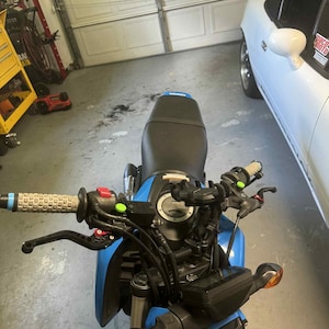 May include: A blue motorcycle with black detailing, including a black seat and handlebars. The motorcycle has a digital display and orange indicators. The image is taken from the rider's point of view.