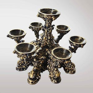 K&ouml;nnte beinhalten: Ein mehrstufiger Kerzenhalter mit sechs kreisf&ouml;rmigen Schalen, die um eine zentrale, erh&ouml;hte Schale angeordnet sind. Die Struktur ist in einer abgenutzten Schwarz-Gold-Optik gehalten und weist verzierte, schn&ouml;rkelartige Details am Fu&szlig; auf.