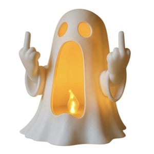 May include: A white ghost-shaped lamp with a hollow centre featuring a warm yellow light. The ghost has two oval eyes and two arms raised, with each hand extending a middle finger. The surface of the lamp has a matte, textured finish.