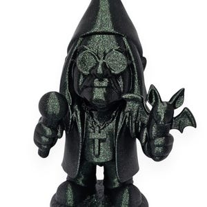 May include: A dark green glittery figurine of a gnome wearing round sunglasses, a long coat, and a cross necklace. The gnome holds a microphone in one hand and a small bat in the other, featuring a pointed hat and long hair, standing on a round base.