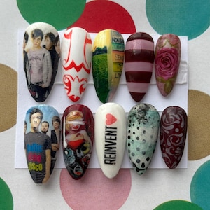 Könnte beinhalten: Ein Set aus zehn künstlichen Fingernägeln mit verschiedenen Designs. Die Designs umfassen Bandfotos, abstrakte Muster, eine Rose und das Wort "REINVENT" mit einem Herz. Die Nägel sind oval und in Farben wie Weiß, Rot und Grün gehalten.