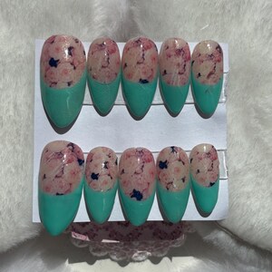 Könnte beinhalten: Set aus zehn künstlichen Nägeln. Jeder Nagel hat ein hellrosa Blumendesign mit blauen Akzenten auf klarer Basis. Die Spitzen sind einfarbig türkis lackiert. Die Nägel sind auf einer weißen Karte angeordnet.