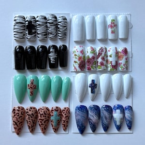 Könnte beinhalten: Eine Sammlung von aufklebbaren Nägeln in verschiedenen Designs. Enthält Zebrastreifen, Kreuze, einfarbiges Schwarz, Blumenmuster, Mintgrün, Leopardenmuster, Galaxien und Weiß mit blauen Kreuzen. Jedes Set ist auf weißem Hintergrund angeordnet.