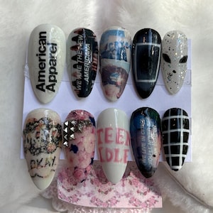 Könnte beinhalten: Ein Set aus zehn künstlichen Nägeln mit verschiedenen Designs. Einige Nägel zeigen Texte wie "American Apparel" und "Teen Idle". Weitere Designs umfassen florale Muster, geometrische Formen und einen Nagel zum Thema Weltraum mit einem Alien-Gesicht.