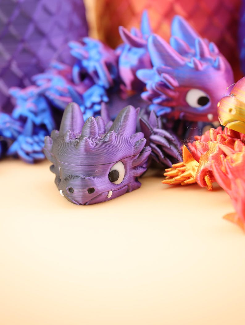 以下が含まれることがあります： カラフルな3Dプリントのドラゴンフィギュアのコレクション。ドラゴンは紫、青、赤、オレンジなど、さまざまな色を特徴としています。各ドラゴンは、スパイクと大きな目を持つ詳細なデザインで、ファンタジーテーマを作成しています。