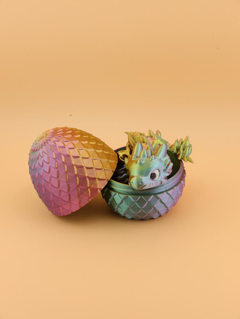 以下が含まれることがあります： 小さなドラゴンフィギュアが現れる、開いた装飾的な卵。卵とドラゴンは虹色で、金色から紫、緑へと色が変化する。卵は鱗のような模様のテクスチャを持っています。
