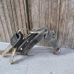 May include: A silver key chain with a horse head design and several keys attached. The keychain is on a wooden surface.