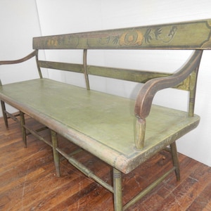 May include: A vintage wooden bench with a distressed green finish. The bench features a backrest with floral accents and curved armrests. The seat is a light green color, and the legs are painted green.