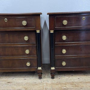 May include: Two matching antique wooden dressers with four drawers each. The dressers are dark brown with black accents and gold-colored hardware. Each dresser has a keyhole on the top drawer.