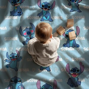 May include: A light blue blanket featuring cartoon images of Stitch, the Disney character, with the name "Sophia" and hearts. A baby is sitting on the blanket with wooden blocks.