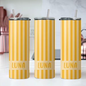 May include: Three tall cylindrical tumblers with lids and metal straws, featuring a vertical yellow and light yellow striped pattern. Each tumbler has a solid light yellow horizontal band near the bottom with the name LUNA printed in yellow.