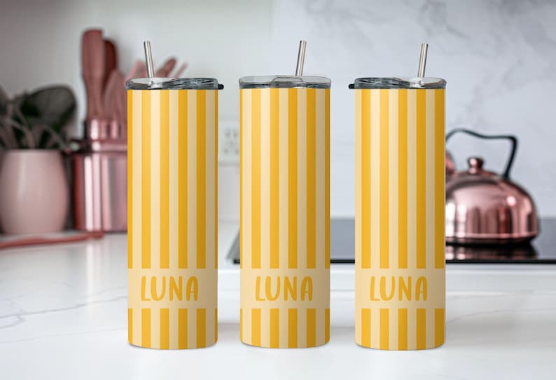 May include: Three tall cylindrical tumblers with lids and metal straws, featuring a vertical yellow and light yellow striped pattern. Each tumbler has a solid light yellow horizontal band near the bottom with the name LUNA printed in yellow.