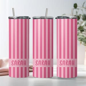 May include: Three tall, cylindrical stainless steel tumblers featuring a vertical pink and light pink striped pattern. Each tumbler has a clear lid with a metal straw and a solid pink horizontal band near the base with the name Sarah in pink.