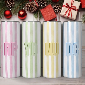 May include: Four stainless steel tumblers with vertical striped patterns in pink, green, yellow, and blue. Each tumbler has a different set of initials cut out of the design. The tumblers are decorated with Christmas ornaments and pine boughs.