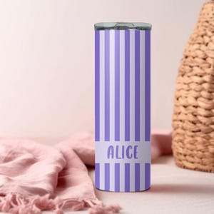 May include: A cylindrical metal tumbler featuring a vertical striped pattern in alternating shades of light purple and white. The lower section of the tumbler includes a solid horizontal band with the name Alice printed in a light purple sans-serif font.