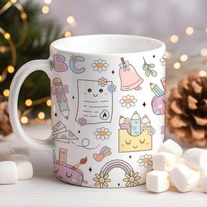 May include: White ceramic mug with a whimsical school-themed design. The mug features colorful illustrations of pencils, a bell, flowers, and a rainbow. The design includes the letters "ABC" and a report card with an "A" grade.