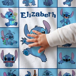 May include: A white blanket featuring a repeating pattern of blue cartoon character images. The word "Elizabeth" is printed in blue. A child's hand is touching the blanket.