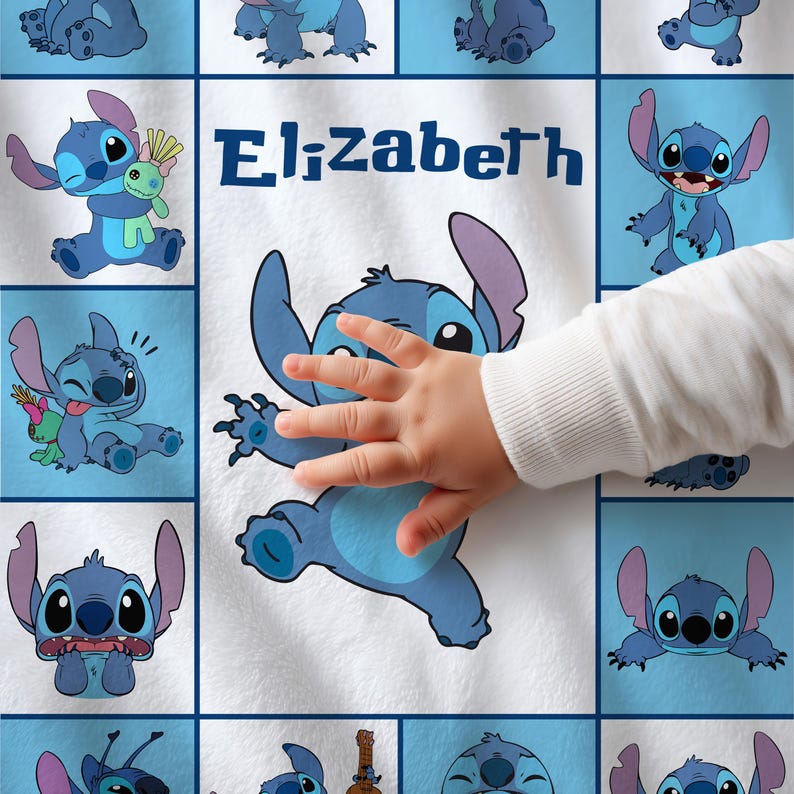 May include: A white blanket featuring a repeating pattern of blue cartoon character images. The word "Elizabeth" is printed in blue. A child's hand is touching the blanket.