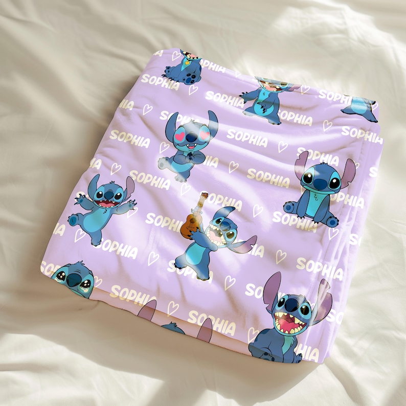 May include: A lavender blanket featuring cartoon character Stitch in various poses. The blanket has the name "SOPHIA" printed repeatedly, along with small heart shapes. Stitch is blue with large ears and a playful expression.