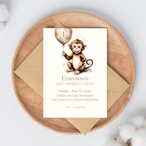 Op de afbeelding: Een witte uitnodigingskaart met een bruine aap die een gouden ballon vasthoudt met het nummer 1 erop. De tekst op de kaart luidt "Emerson's First Birthday Party! Sunday June 14 | 2 pm 123 Lions Den Lane, Wateringhole Come dressed as your favourite Safari Animal RSVP: 123-456-7890"