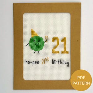 Puede incluir: Tarjeta de cumpleaños bordada con un personaje de guisante verde con gorro de fiesta y copa de champán, celebrando el 21 cumpleaños. La tarjeta tiene el texto "ha-pea 21st birthday" y está enmarcada en marrón.