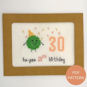 Könnte beinhalten: Gestickte Geburtstagskarte mit einer grünen Erbsenfigur mit Partyhut und der Zahl 30. Der Text lautet "ha-pea 30th birthday" in Schwarz und Pfirsich. Die Karte befindet sich in einem braunen Rahmen.