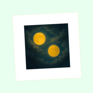 May include: A digital art print depicting two large, yellow moons shining through a dark, cloudy sky. The moons are the central focus, with a soft, ethereal glow. The print is framed in a white mount.