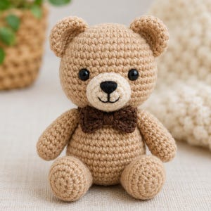 Könnte beinhalten: Ein kleiner, hellbrauner gehäkelter Teddybär mit einer cremefarbenen Schnauze, schwarzen Kunststoffaugen, einer gestickten schwarzen Nase und einem Mund sowie einer dunkelbraunen, gehäkelten Fliege am Hals. Der Bär sitzt aufrecht.