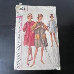 May include: Vintage Simplicity sewing pattern 6074 featuring illustrations of three dresses. The pattern includes measurements for a medium size, bust 34-36 inches. The cover is white with pink and yellow accents.