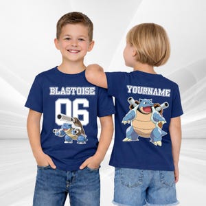 Puede incluir: Dos camisetas azul marino con un diseño de dibujos animados de Blastoise. La parte delantera de las camisetas muestra "BLASTOISE 06" en letras blancas. La parte trasera de una camiseta tiene "YOURNAME" y la otra el personaje de Blastoise.