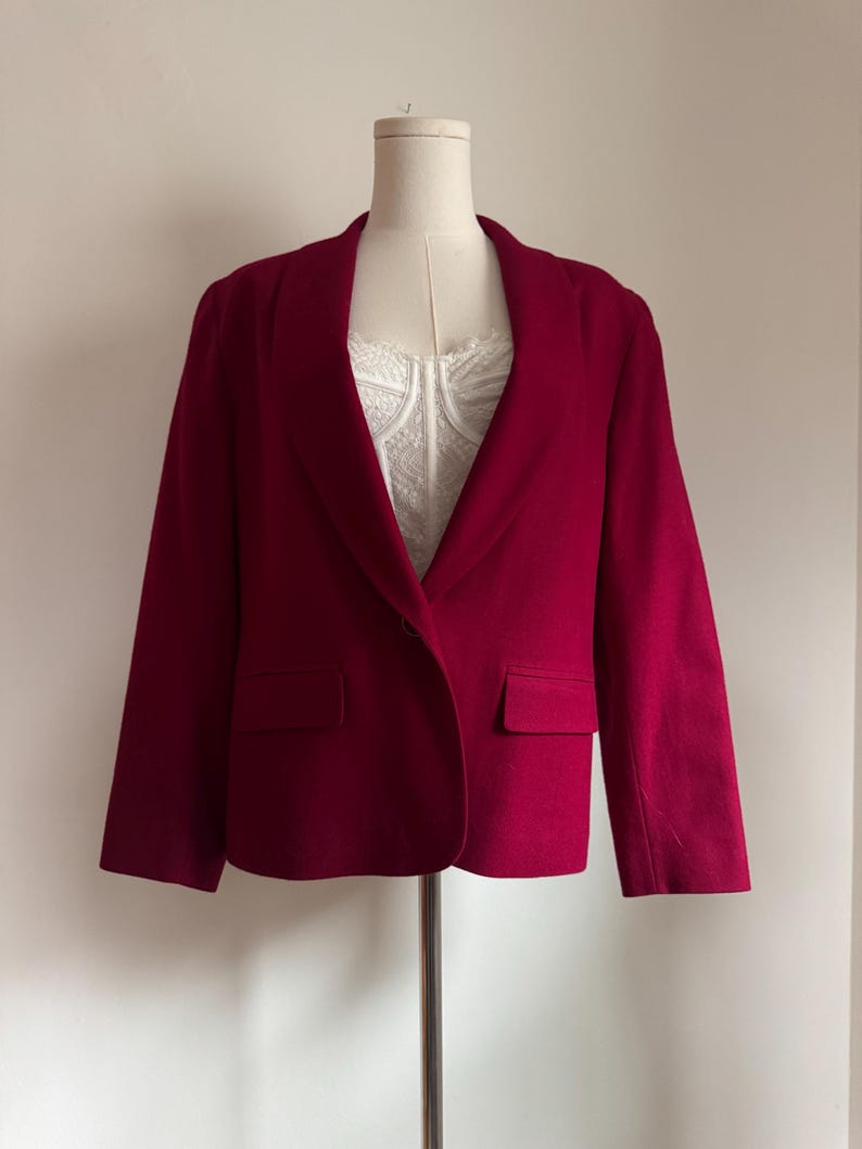 Pu&ograve; includere: Un blazer rosso scuro con revers a lancia e due tasche anteriori. Il blazer &egrave; esposto su un manichino, mettendo in risalto la sua vestibilit&agrave; su misura e il design classico. Il capo ha maniche lunghe e una chiusura con un solo bottone.