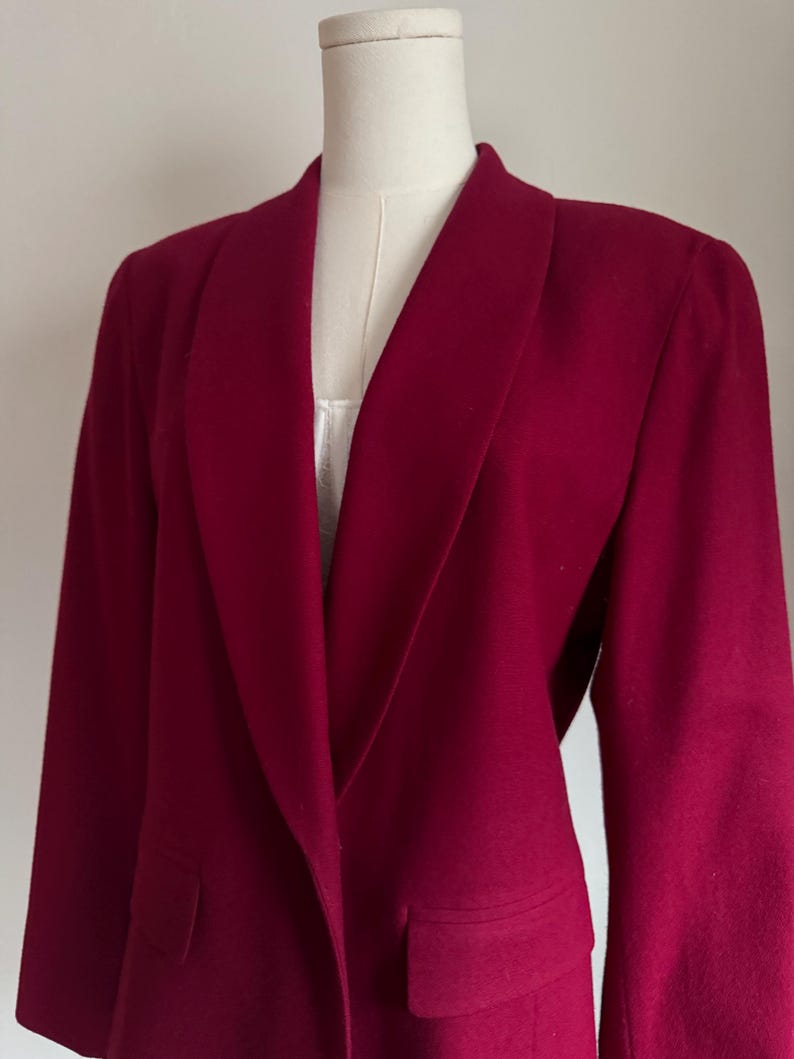 Pu&ograve; includere: Un blazer rosso intenso con un ampio colletto a revers e due tasche frontali. La giacca a maniche lunghe &egrave; esposta su un manichino. Il blazer &egrave; realizzato in un tessuto morbido e strutturato.