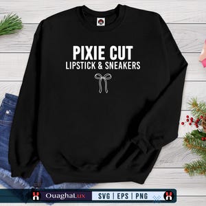Puede incluir: Sudadera negra con el texto blanco "PIXIE CUT LIPSTICK & SNEAKERS" y un lazo blanco. La imagen incluye pantalones cortos de mezclilla, una caja de regalo y vegetación festiva.
