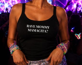 Może przedstawiać: Czarny top na ramiączkach z białym napisem RAVE MOMMY MAMACITA? nadrukowanym na klatce piersiowej. Odzież posiada okrągły dekolt i szerokie ramiączka. Wzór jest wyśrodkowany na przodzie koszulki, noszonej z kolorowymi bransoletkami z koralików.