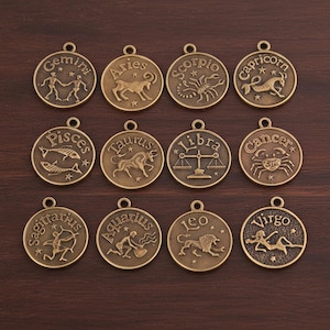 May include: Twelve bronze-colored zodiac sign pendants. Each pendant features a different zodiac symbol and name, including Gemini, Aries, Scorpio, Capricorn, Pisces, Taurus, Libra, Cancer, Sagittarius, Aquarius, Leo, and Virgo.