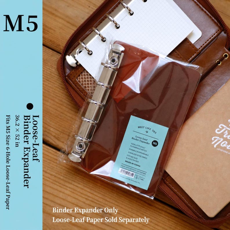 May include: A silver-colored metal loose-leaf binder expander with six rings, packaged in a clear plastic sleeve. The label reads M5 Loose-Leaf Binder Expander, 36.2 x 52 in, fits M5 size 6-hole loose-leaf paper. The expander is shown inside a brown leather-like zippered binder.