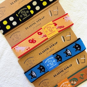 May include: An assortment of elastic straps for notebooks, each with a unique design. The straps feature patterns like polka dots, floral motifs, and animal illustrations. Each strap is 25mm wide and 130mm long, with the text "ELASTIC STRAP for notebook".