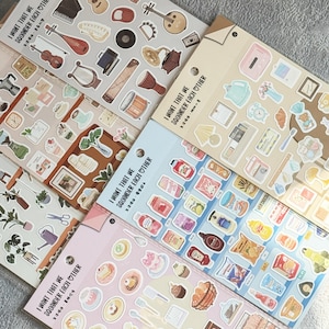 May include: A collection of sticker sheets featuring various themed designs. The stickers include musical instruments, food items, plants, and household objects. The text "I WANT THAT WE SQUANDER EACH OTHER" is printed on each sheet.