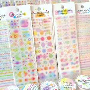 May include: A collection of colorful sticker sheets and matching washi tape rolls. The sticker sheets feature various designs, including dots, shapes, and hearts, in a pastel rainbow palette. The washi tape rolls have coordinating designs and text.